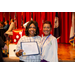 A women with her award posing with another individual with various flags in the background.