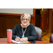 A woman holding a pen while sitting a speaking with someone out of frame.