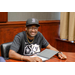 An individual in a baseball cap and glass sitting the table smiling big at someone out of frame.