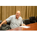 A man with a stack of papers sitting at a table smiling at the camera.