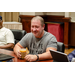 A man with cold drink sitting and listening to someone that is speaking out of frame.