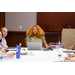 A woman with a laptop listening to someone speak at the other end of the table.