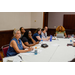 A wide shot of the table with several individuals listening to someone out of frame.