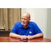 A man in a royal blue shirt sitting and leaning on the table thinking about what is being said.