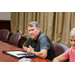 A man leaning forward on the table listening to someone across and down the table from him.