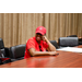 A woman in a red shirt and hat smiling at someone out of frame further down the table.