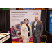 A man and a woman posing in front of a banner that says AMA: Creating a better way to advance people and performance. Your Agency of choice in management, consulting, and compliance.