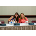 Two women sitting at a table behind state name plates: one Virginia and one West Virginia.