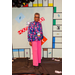 A woman in pink pants and a pink, blue, red, and green floral shirt posing in the Housingopoly game board photo booth.