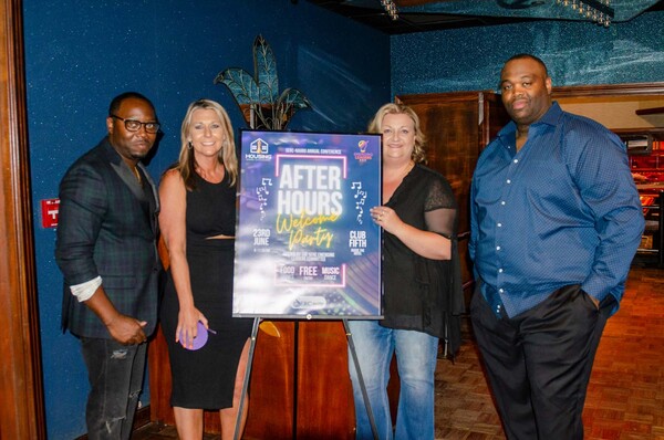 Four individuals standing next to a poster that says After Hours Welcome Party.