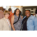 Three women smiling big for the camera with various individuals enjoying the International Civil Rights Center and Museum behind them.