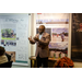 Treasurer James Cox gesturing with his hands to a crowd while standing in front of several posters hanging on the wall.