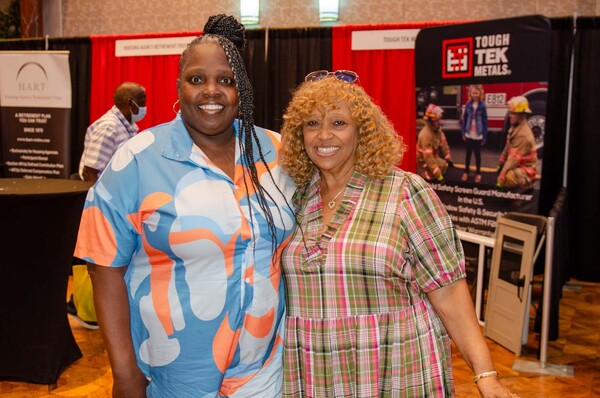 Two women posing in front of the Tough Tek Metals booth.