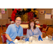 A man and a women sitting at a dining table with a red, black, and gold balloon arch in the background.