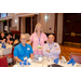 A woman standing behind two men that are sitting at a dining table.