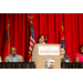 A woman speaking at the podium with the rest of the panel sitting on either side.