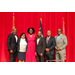 President Anthony Goodson, Jr. and Treasurer James Cox taking a group photo with four other individuals in front of a red curtain and three flags.