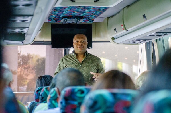 President Anthony Goodson, Jr. at the front of a bus speaking to the passengers sitting down in their seats.