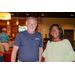 A man and a woman smiling for the camera with a bar tender making a drink in the background.