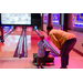 A child using a ramp to roll a bowling ball down a lane while a woman stands next to him.