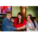 Three women sitting at a booth with various bowling balls in the background.