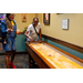 A woman playing table shuffleboard with another standing off to the side watching.