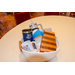 A white rope gift basket filled with tumblers, a candle, a mug, and a wooden cutting board.