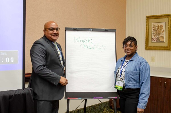 A woman and a man standing next to an easel note pad with the words Work Orders.