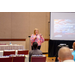 A woman speaking into a microphone while giving a presentation to a crowd.