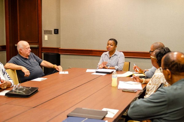 A woman sitting at the head of a table speaking to five other individuals.