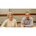 A woman in a white sweater and a man in a blue button up smiling for the camera.