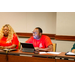 A man in a red shirt with a tablet, listening to a speaker.