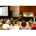 A wide shot of a speaker talking to a crowd sitting at tables.