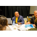 President Anthony Goodson, Jr. wearing a yellow shirt with a blue blazer sitting at a table listening to someone speak.