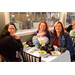 Three women sitting at a small dining table eating salads.