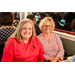 Two women sitting at a table and smiling big for the camera.