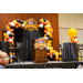 A stage with a podium that says SERC, Game day, a balloon arch, and two round tables with chairs.