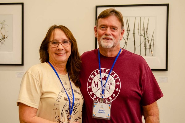 A woman in a beige faith shirt standing next to a man in a red Medieval Times shirt.