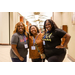 Three woman standing in a hallway smiling big for the camera.