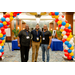 Three men taking a group photo under a balloon arch.