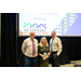 A woman and two men standing in front of a projector screen that says A.H. Forward November 2024.