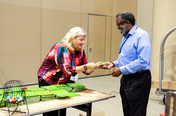 A woman handing out a Bingo card to an individual.