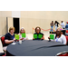 Four women sitting at a table while holding up their filled in Bingo cards.