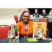 A woman in an orange shirt holding a wine set and a gift bag with a cutting board, tumbler, and gift card in it.