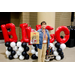 A woman in a jean jacket holding up a gift bag in front of the Bingo balloon arch.