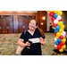 A woman in a black shirt holding a check while standing underneath a balloon arch.