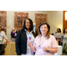 A woman in a pink shirt holding out a Visa gift card to a woman in a black blazer.